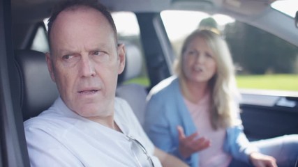 Mature couple argue in the car as husband looks away annoyed - Powered by Adobe
