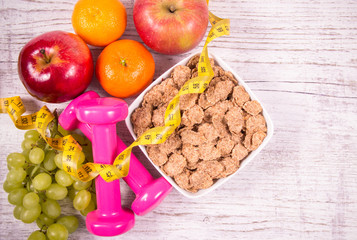 Diet fitness concept - dumbbells, measuring tape, flakes and fresh fruits on wooden table.