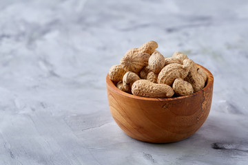 Unpeeled peanuts in wooden plate over white textured background closeup, selective focus