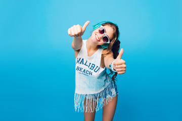 Pretty girl with long curly hair in tail in blue sunglasses  on blue background in studio. She...