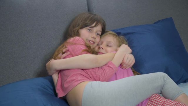 funny sisters fooling around on bed. two girls hugging and clinch each other. funny faces and pose