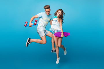 Young couple having fun on blue background in studio. They wear T-shirts, jeans shorts. They are...