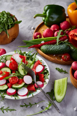 Creative fresh vegetable salad with ruccola, cucumber, tomatoes and raddish on white plate, selective focus