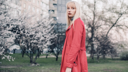 Young blonde woman goes for walk in spring garden on background of blossoming trees.