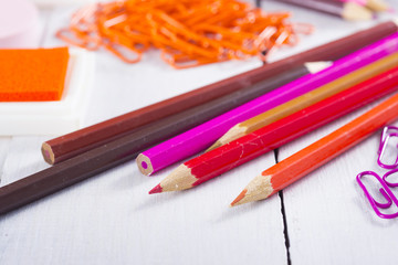 Obraz premium red, pink, purple color pencils and paper clips, ink pads on white wooden table background