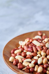 Raw mixed peanuts in wooden plate isolated over white textured background, top view, close-up.