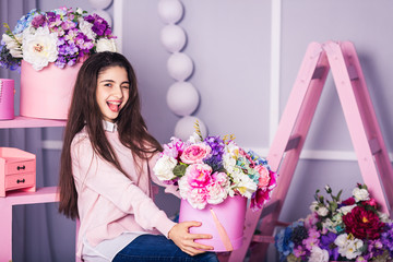 Beautiful girl in jeans and pink sweater in studio with decor of flowers in baskets.