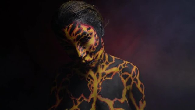 Body painting on the body of a girl in the form of volcanic lava, around which there is smoke on a red background