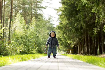 Happy smiling one year baby boy on the walk in the sunny summer park or forest. Concept of first steps