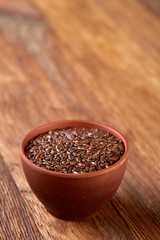 Flax seeds in wooden bowl on rustic wooden background, top view, selective focus