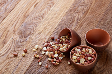 Fototapeta na wymiar Two ceramic bowls with raw peanuts mix isolated over rustic wooden backround, top view, close-up.