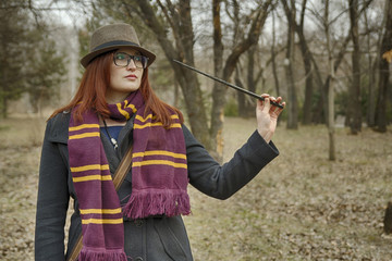 A witch girl with a magic wand in her hand, wearing glasses, a coat, a hat and a scarf, with a vintage bag, pronounces a spell