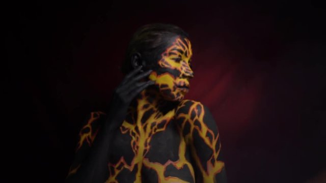 Bodyart on the body of the girl in the form of a current magma through the earth, which passes her fingers over her lips and turns away in the other direction