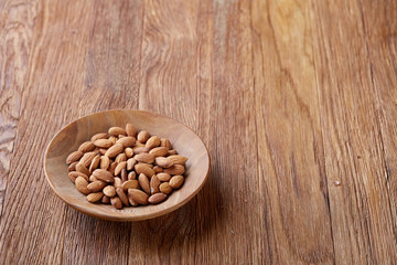 Tasty almond on a wooden plate over wooden background, top view, close-up, selective focus.