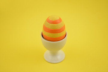 Easter striped egg stock images. Spring decoration images. Ceramic egg stand with yellow egg. Easter decoration on a yellow background