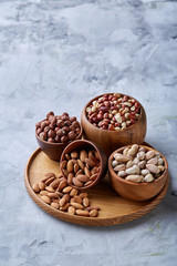 Mixed nuts in brown bowls on wooden tray over white background, close-up, top view, selective focus.