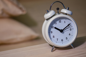 white alarm clock on side table with pillow in background