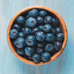 Blueberries in a wooden bowl on bright blue wooden table. Top view, close up.