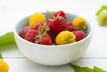 red and rare yellow raspberry fruits on white wooden table background