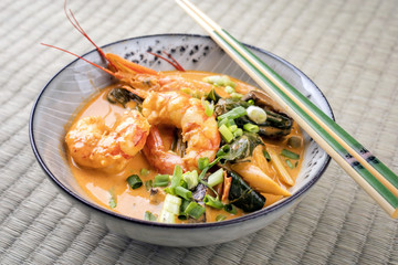 Traditional Thai kaeng phet red curry with king prawns and vegetable as top view in a bowl on place mat