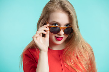 Close up shot of stylish young woman in sunglasses smiling against blue background. Beautiful female model with copy space.