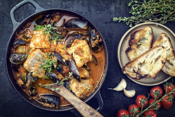 Traditional French Corsican fish stew with mussels and garlic baguette as top view in a pot