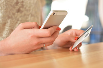 Hands of a girl with a mobile smartphone and a credit card on a wooden table. Internet banking, the concept of online trading, the concept of e-commerce.