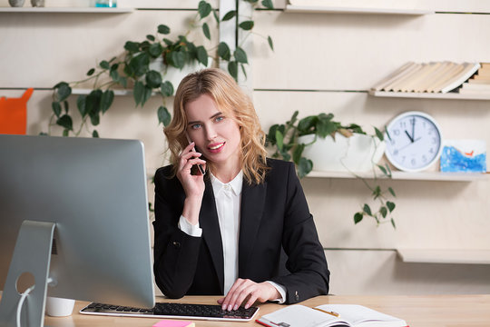 Business woman working on computer and speking over phone with partner.