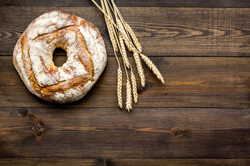 Home bread with classic recipe. Round loaf near ears of wheat on dark wooden background top view copy space