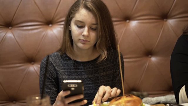 Two teenage girlfriends staring at smartphones sitting in cafe

