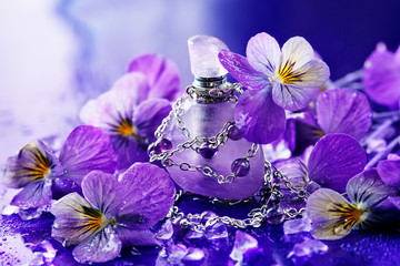 Essential oil bottle made of amethyst stone. Perfume bottle surrounded by violets flower petals. Floral cosmetics, botanical fragrance concept. 