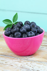 Fresh nutritious blueberries in pink bowl on wooden surface
