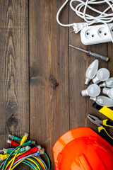 Electrician work concept. Hard hat, tools, cabel, bulb, socket outlet on dark wooden background top view space for text
