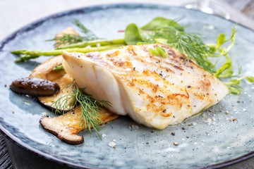 Gebratenes Kabeljaufilet mit grünem Spargel und Champignons als Nahaufnahme auf einem Teller