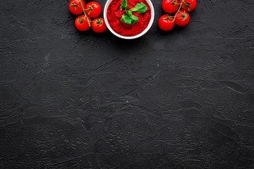 Tomato sauce in bowl with green basil near cherry tomatoes on black background top view space for text