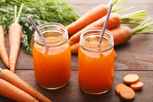 Fresh carrot juice in glass jars on brown wooden background