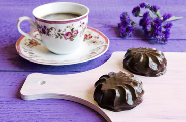 Marshmallows in Chocolate on white cutting board and cup of coffee on Violet wooden background