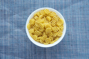 Macaroni ruote Pasta in a white cup on a blue knitted background in the center. Close-up with the top.