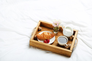 Tasty breakfast in bed on wooden tray