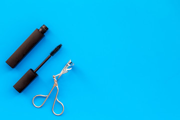 Basic products for eyelashes makeup. Mascara and eyelash curler on blue background top view copy space
