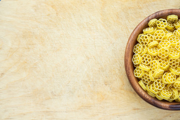 Macaroni ruote pasta in a wooden bowl on a wooden table textured background with a side. Close-up with the top. Free space for text.