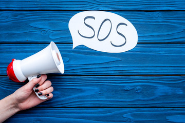 Ask for help concept. Megaphone near cloud with word SOS on blue wooden background top view copy...