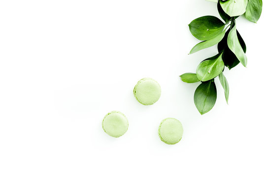 Summer background with green leaves and sweets macarons on white top view copy space