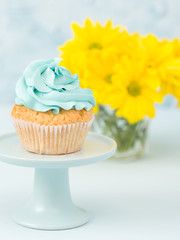 Cupcake with blue cream decoration on vintage stand and bouquet of yellow chrysanthemum in glasses vase.