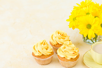 Cupcake with yellow cream decoration, coffe with milk and bouquet of yellow chrysanthemum in small glasses cup.