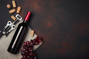 Bottle of wine, red grapes, corkscrew and corks, on rusty background top view