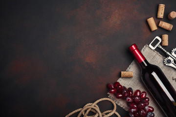 Bottle of wine, red grapes, corkscrew and corks, on rusty background top view