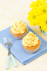 Cupcake with yellow cream decoration on blue napkin and bouquet of yellow chrysanthemum in small glass.