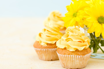 Cupcake with sweet yellow cream decoration and bouquet of yellow chrysanthemum in small glass