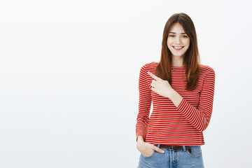 Pleasant attractive girl showing way out. Portrait of friendly confident european girlfriend with positive attitude, pointing at upper left corner and smiling happily, indicating at excellent place